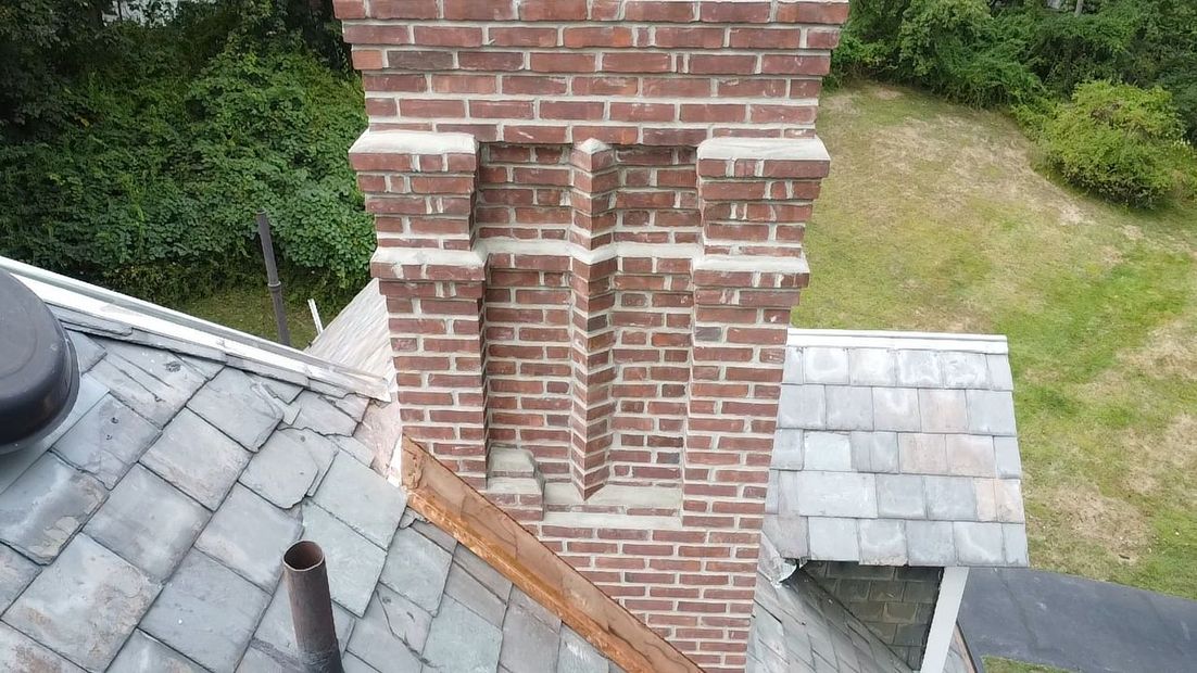 Brick chimney with white trim on a gray shingled roof, viewed from above beside a grassy yard