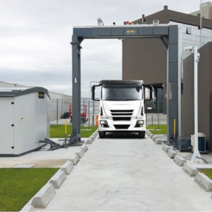 White truck in a concrete weighbridge lane with overhead gantry and roadside equipment at an industrial site