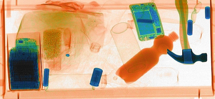 Airport security x-ray of bag contents, showing a laptop, shoes, bottles, and small items in blue and orange.