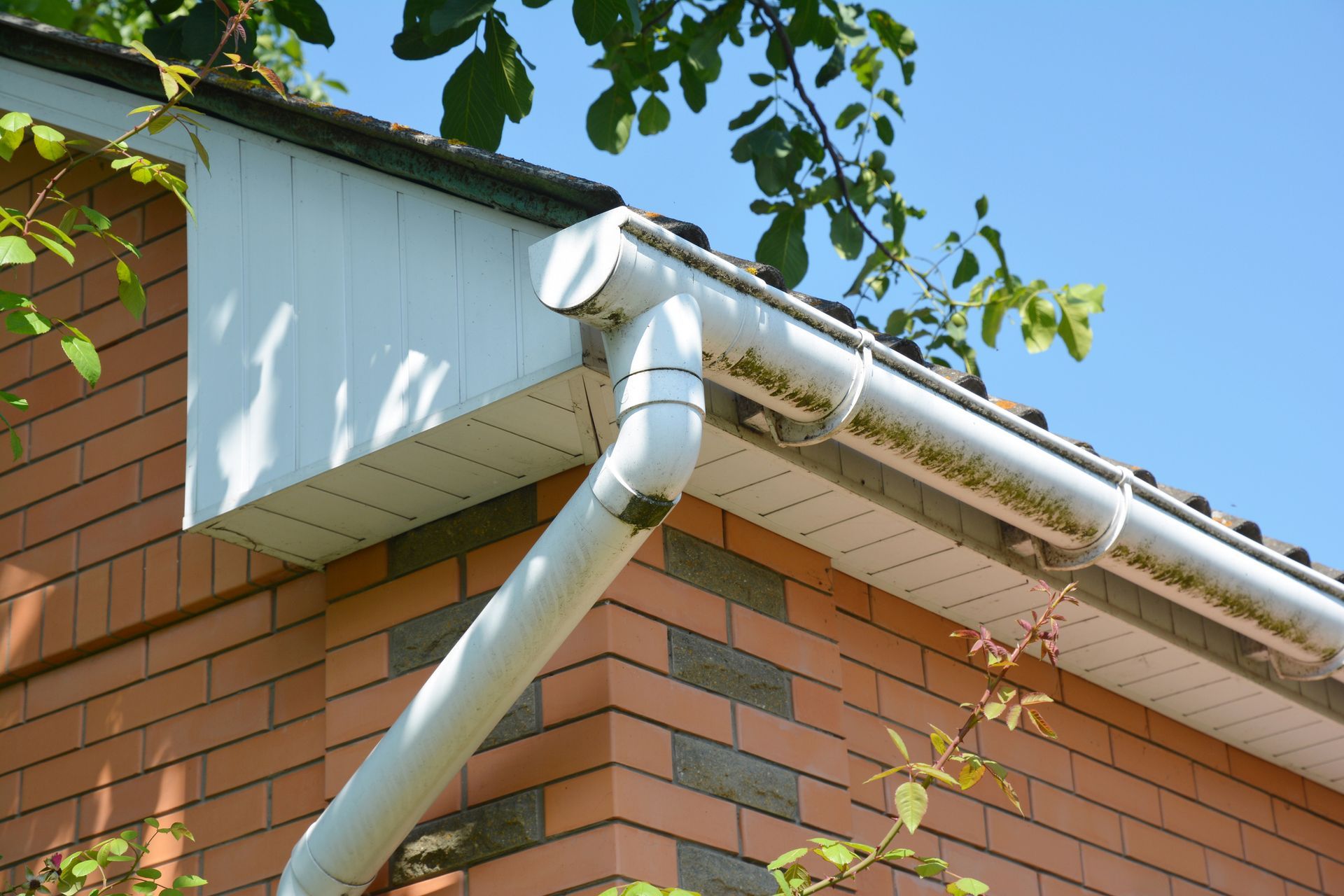 White gutter and downspout on a brick building with white siding, under a blue sky.
