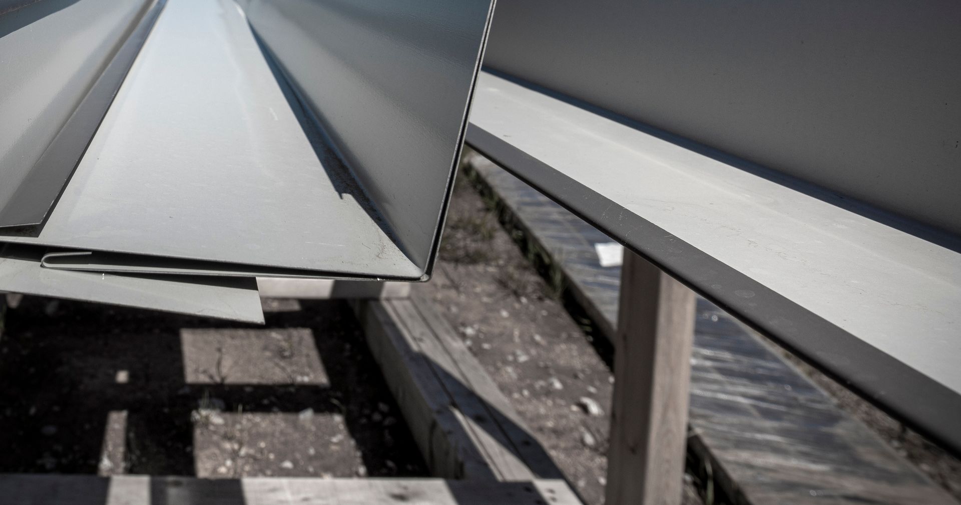 Close-up of stacked, angled metal flashing, likely for roofing, on wood supports in an outdoor setting.