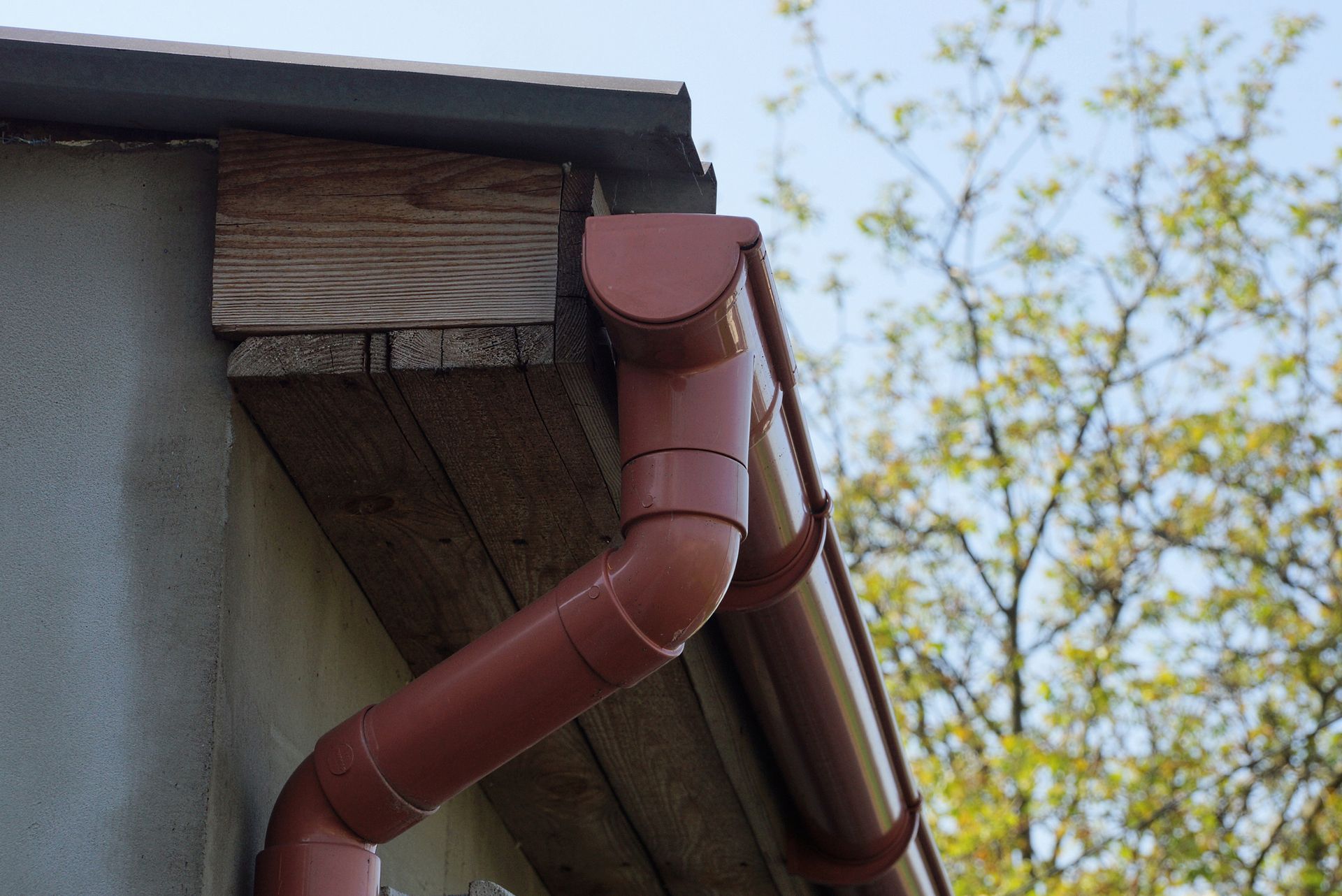 Brown gutter and downspout on a wooden eaves.