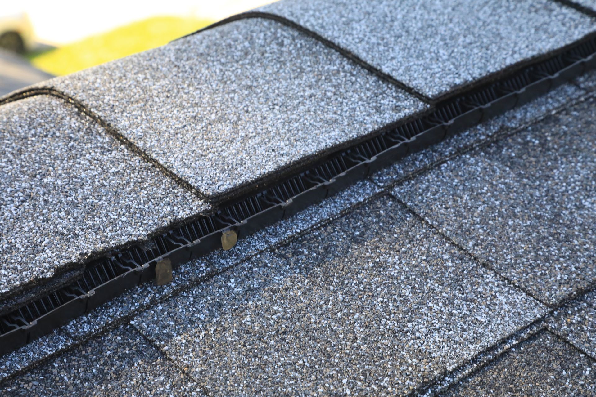 Close-up of a dark grey asphalt shingle roof with a ridge vent installed along the peak.