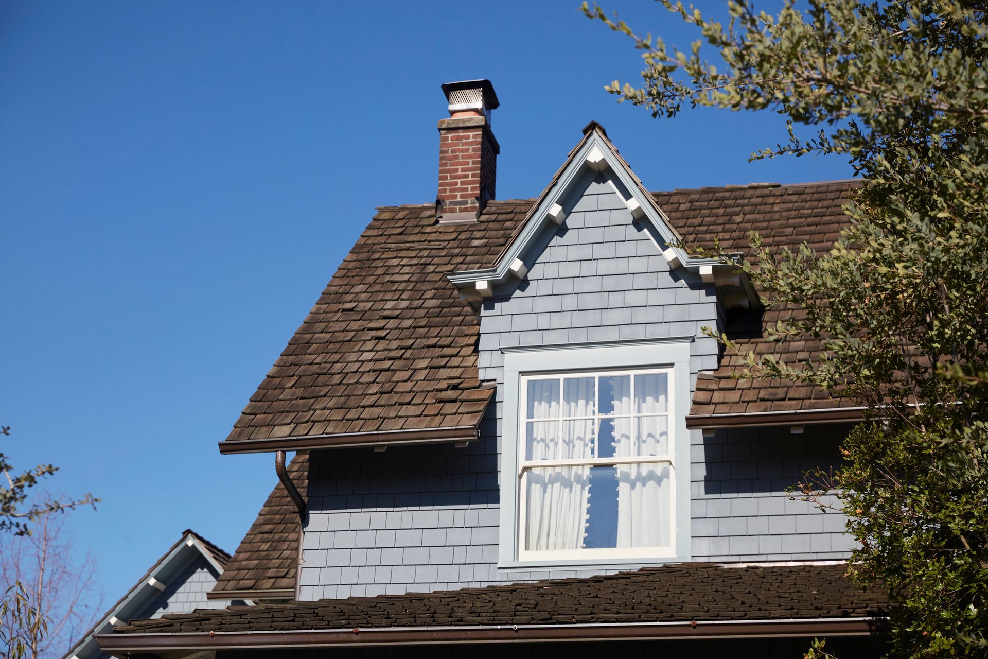 Blue house with brown roof, dormer window, and brick chimney against a blue sky.