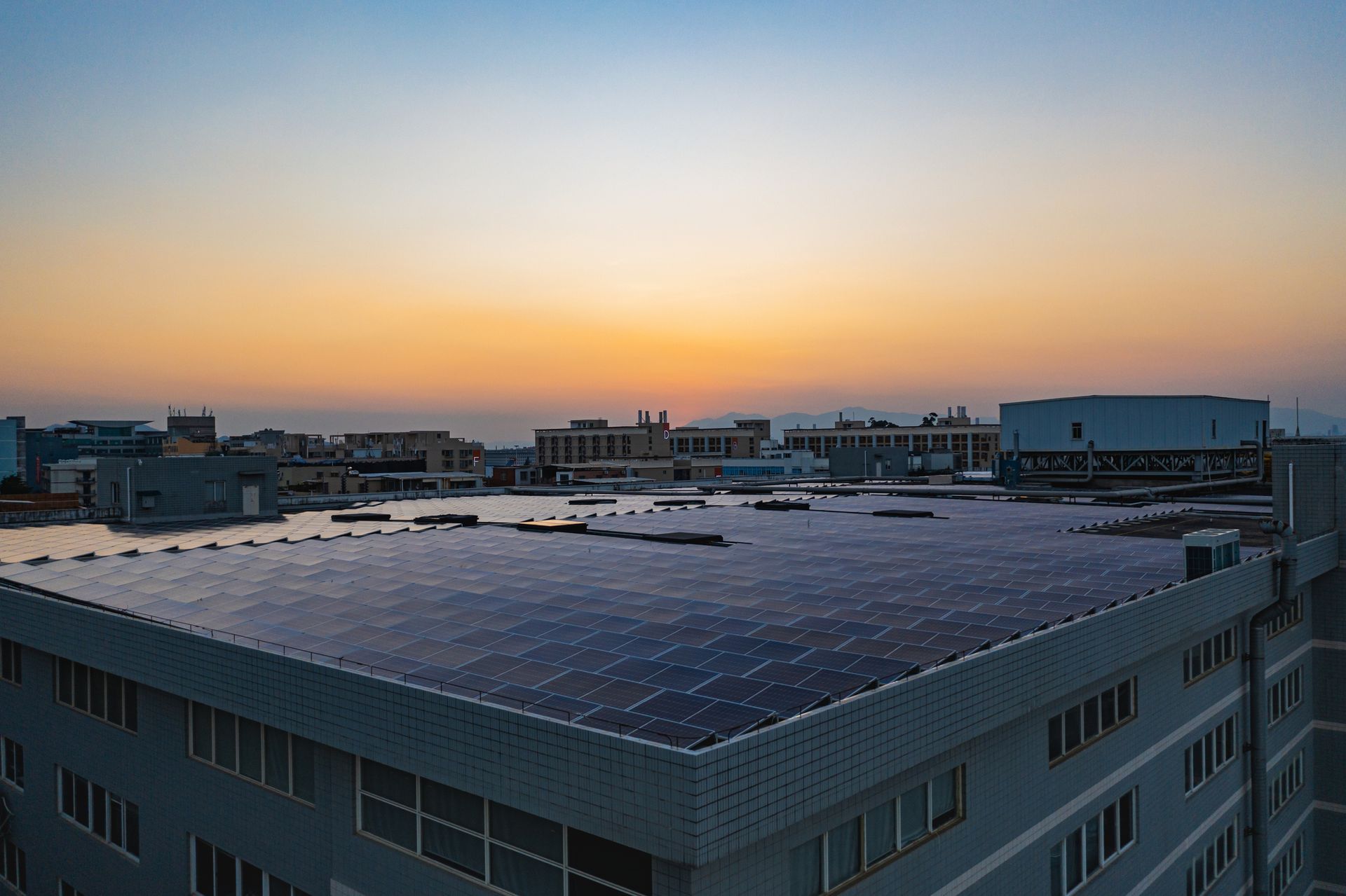 Rooftop solar panels on a building at sunset. The sky is orange and blue.