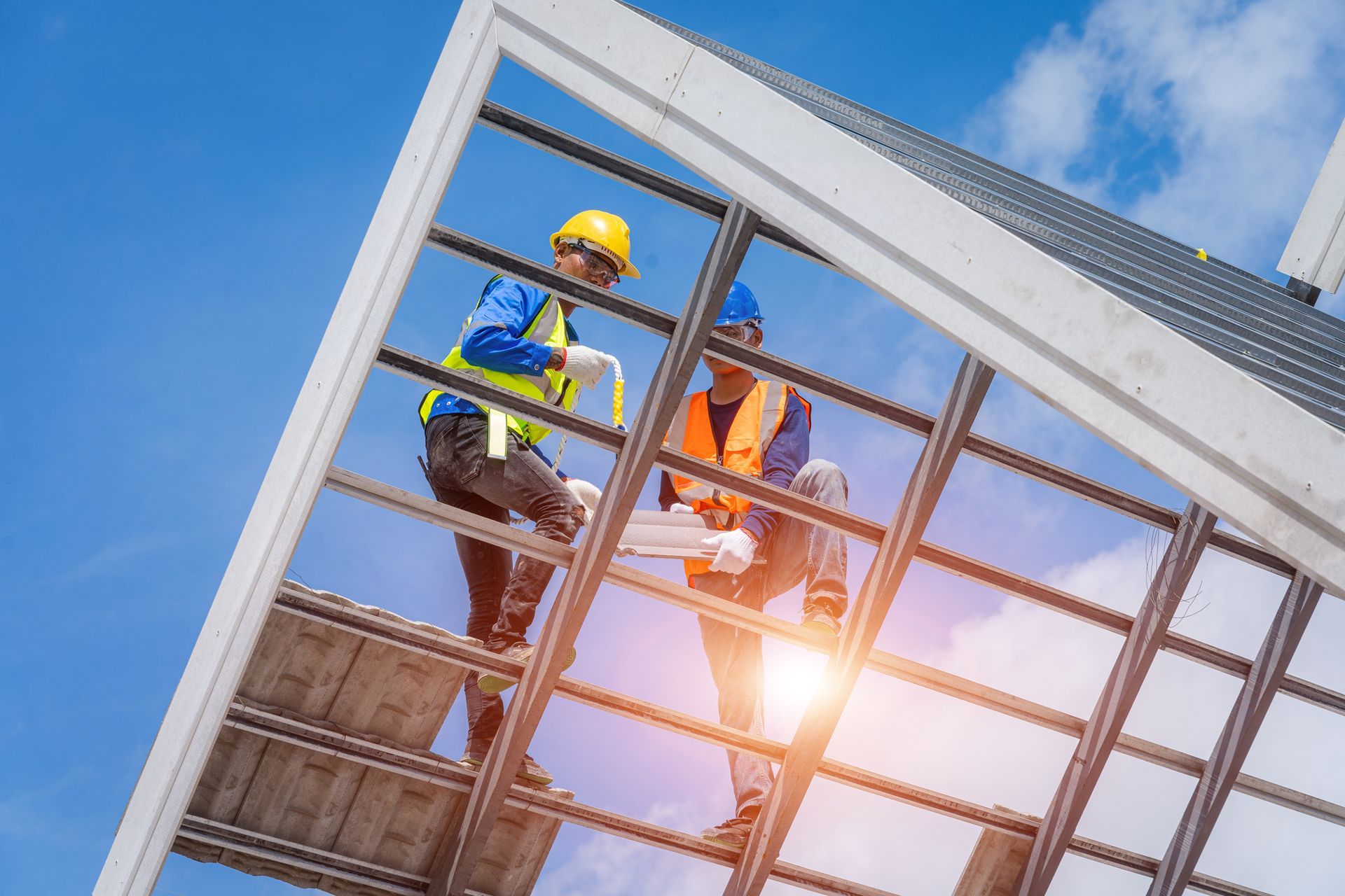 Construction workers on rooftop with blueprints, under blue sky. One in yellow hard hat, other in blue.