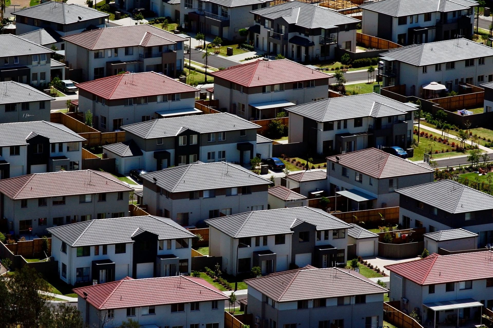 Aerial view of suburban houses with gray and red roofs, neatly arranged with small yards.