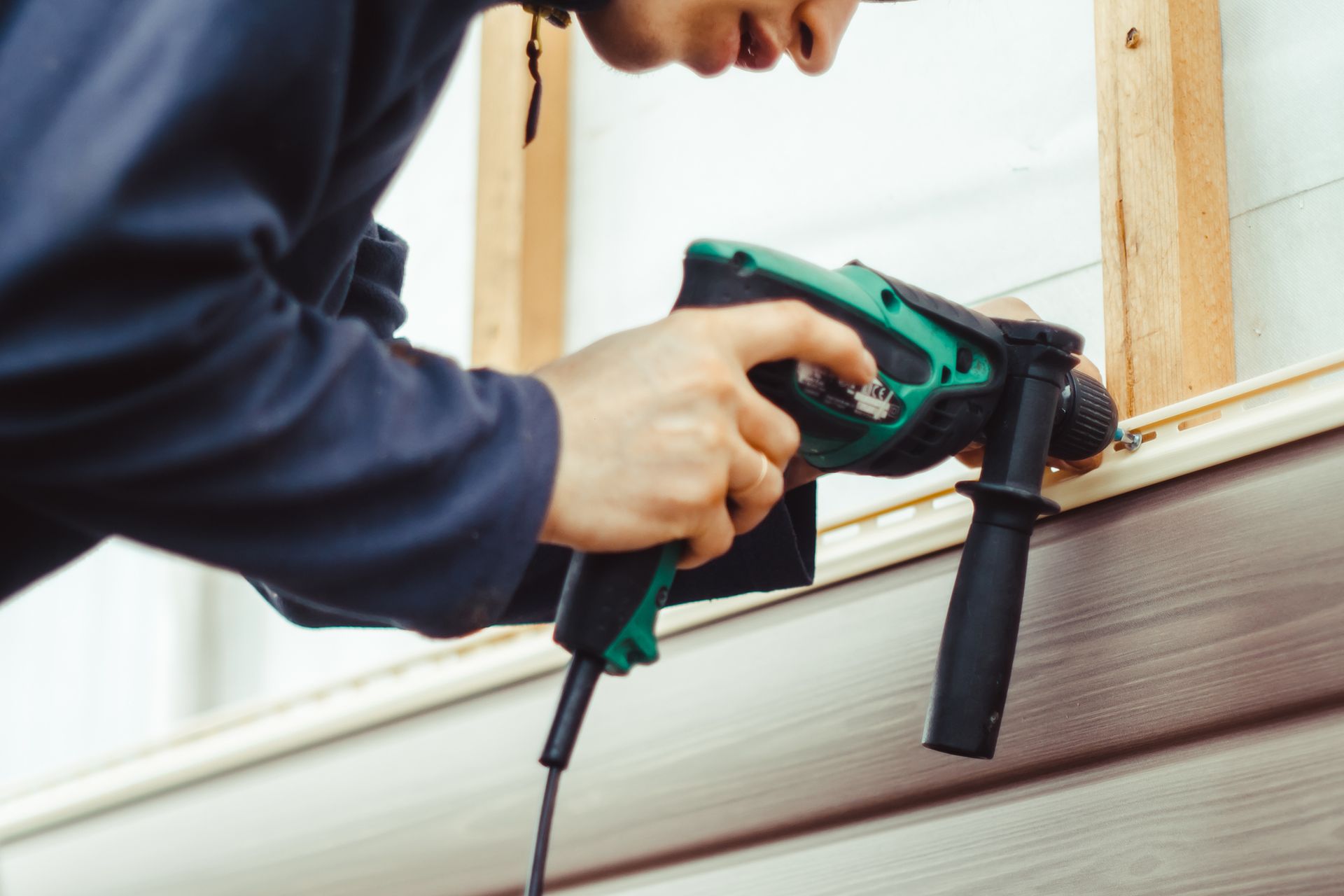 Person using a green drill to work on siding on a building.