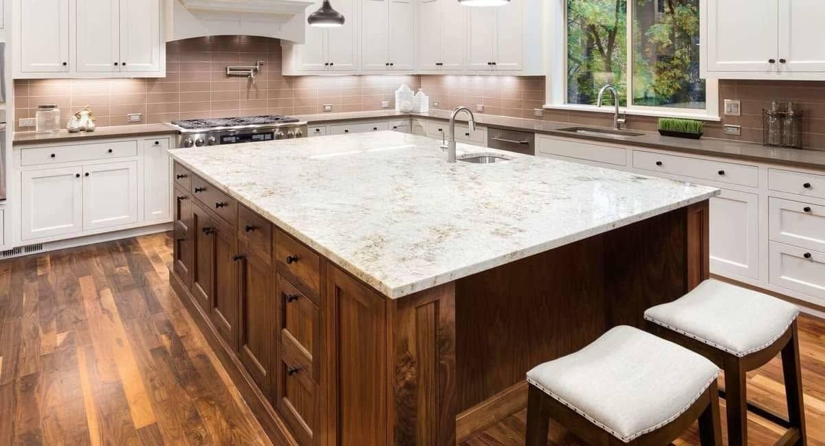 Bright kitchen with a large marble island, white cabinets, wood flooring, and two stools by the counter
