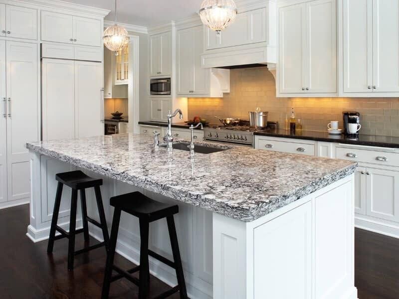Bright white kitchen with granite island, black stools, and stainless steel appliances