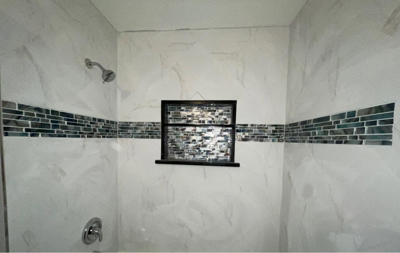 White tiled shower with a horizontal mosaic accent strip and a small black-framed window.