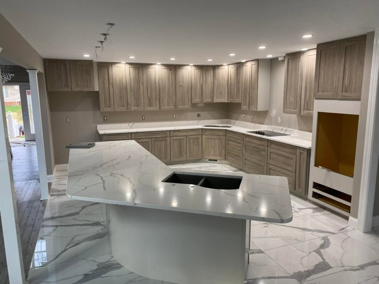 Modern kitchen with white marble island, light wood cabinets, and built-in oven alcove