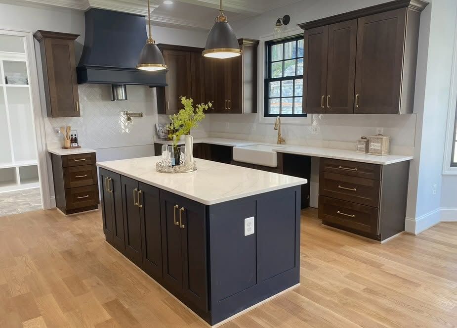 Modern kitchen with dark cabinets, white island countertop, pendant lights, and hardwood floors