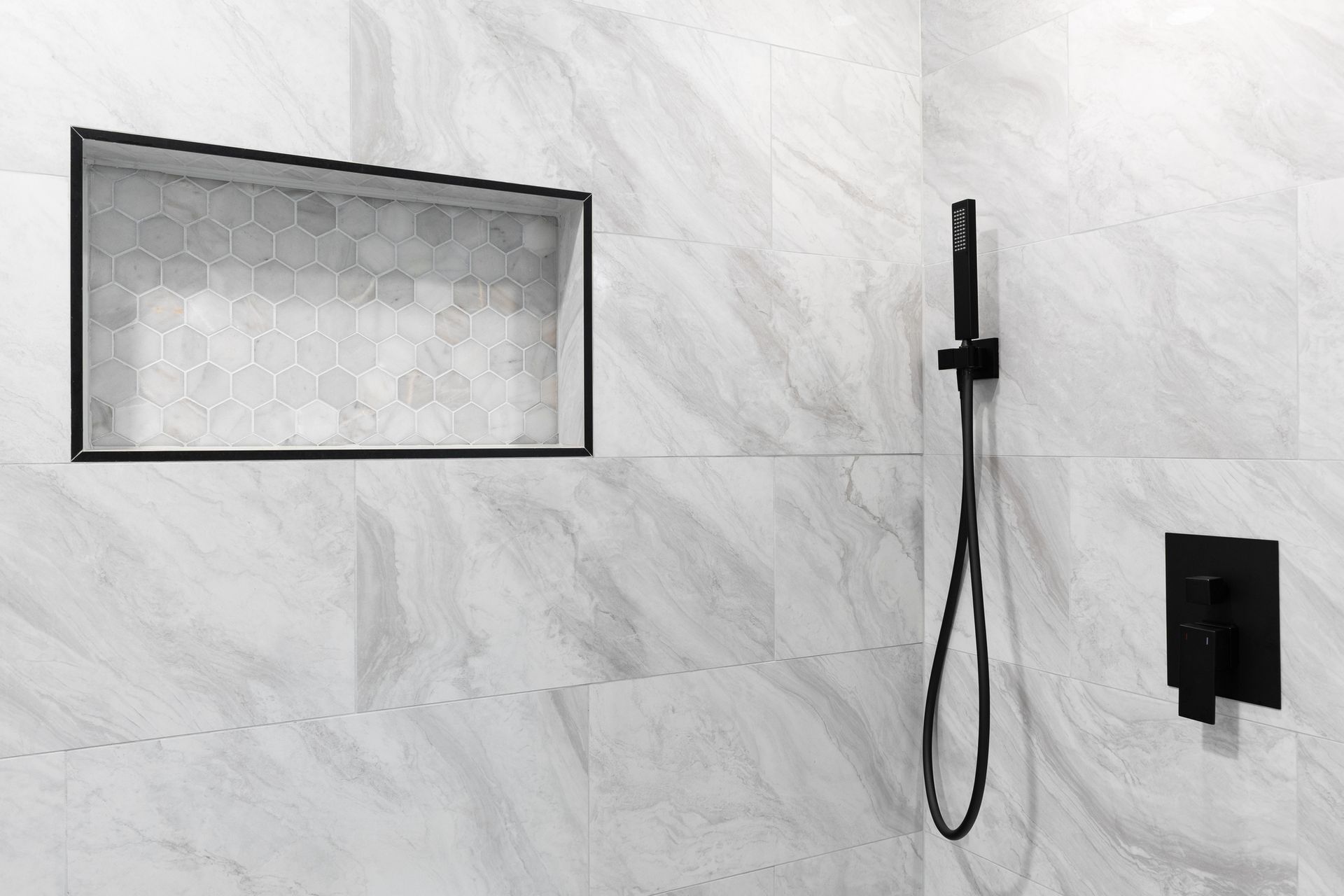 Modern shower with tiled wall, glass shelf, handheld showerhead, and wall controls