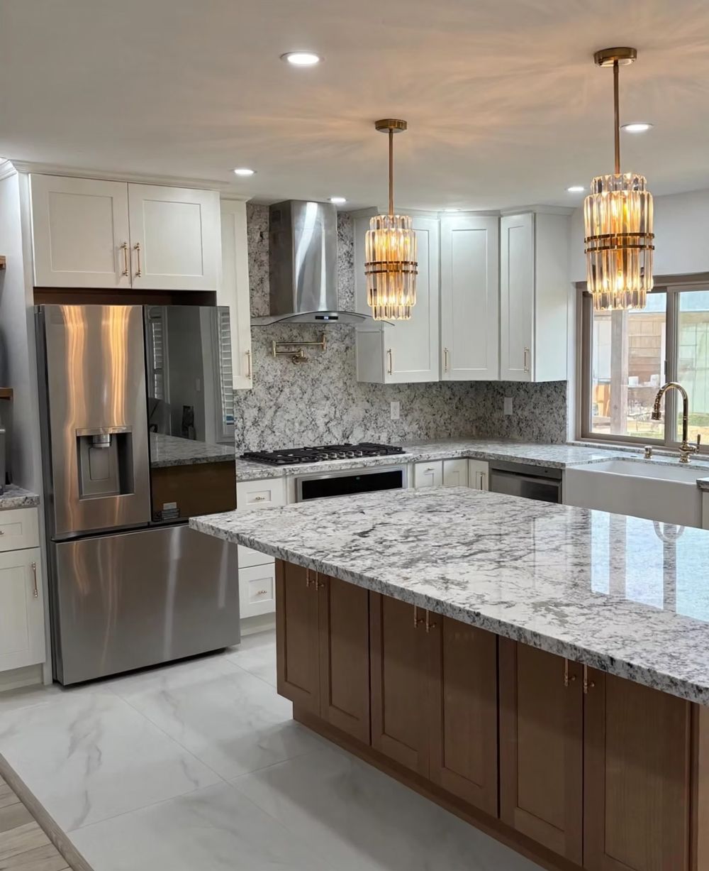 Modern kitchen with white cabinets, stainless fridge, marble countertops, and pendant lights.