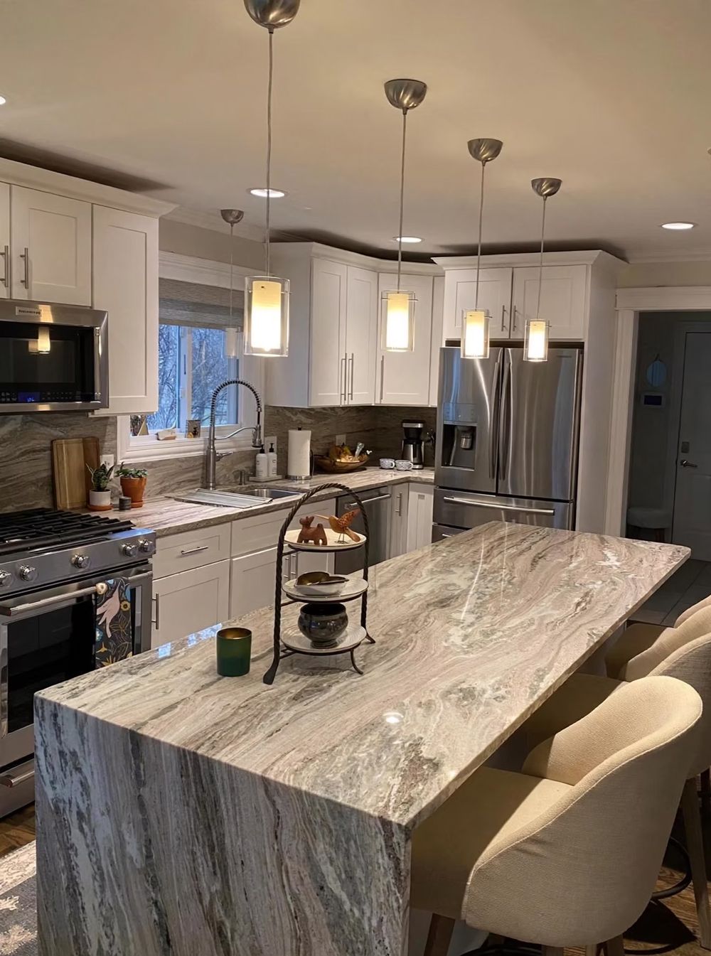 Modern kitchen with marble island, white cabinets, stainless appliances, and pendant lights