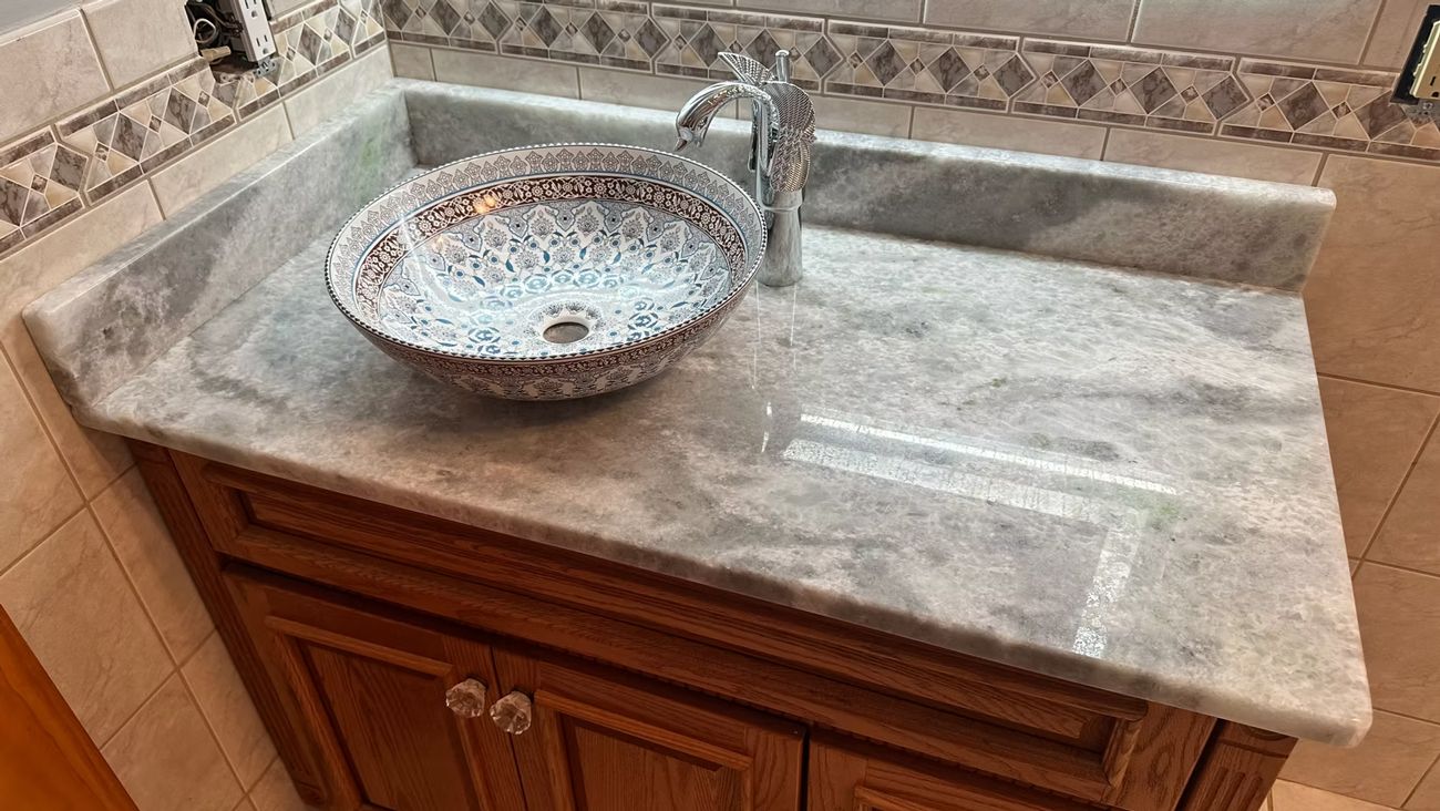 Brown bathroom vanity with granite countertop, round mosaic vessel sink, and chrome faucet against tiled backsplash