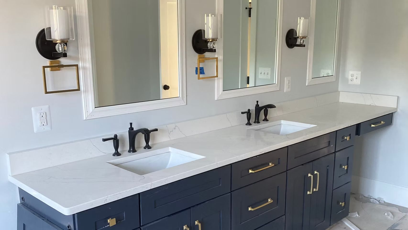 Modern bathroom vanity with double sinks, dark cabinets, white countertop, and mirrors with wall sconces