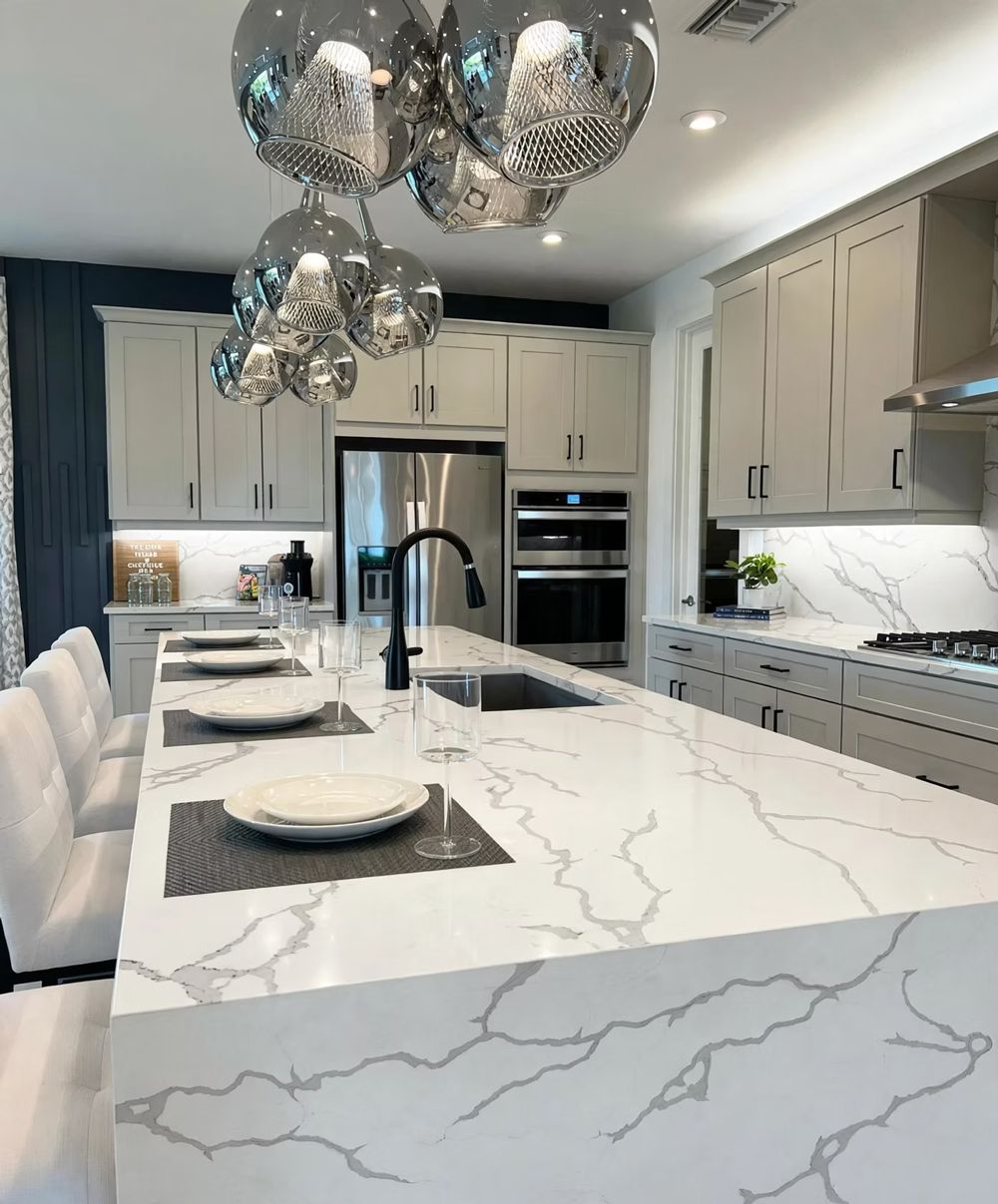 Bright modern kitchen with marble island, silver pendant lights, gray cabinets, and stainless steel appliances