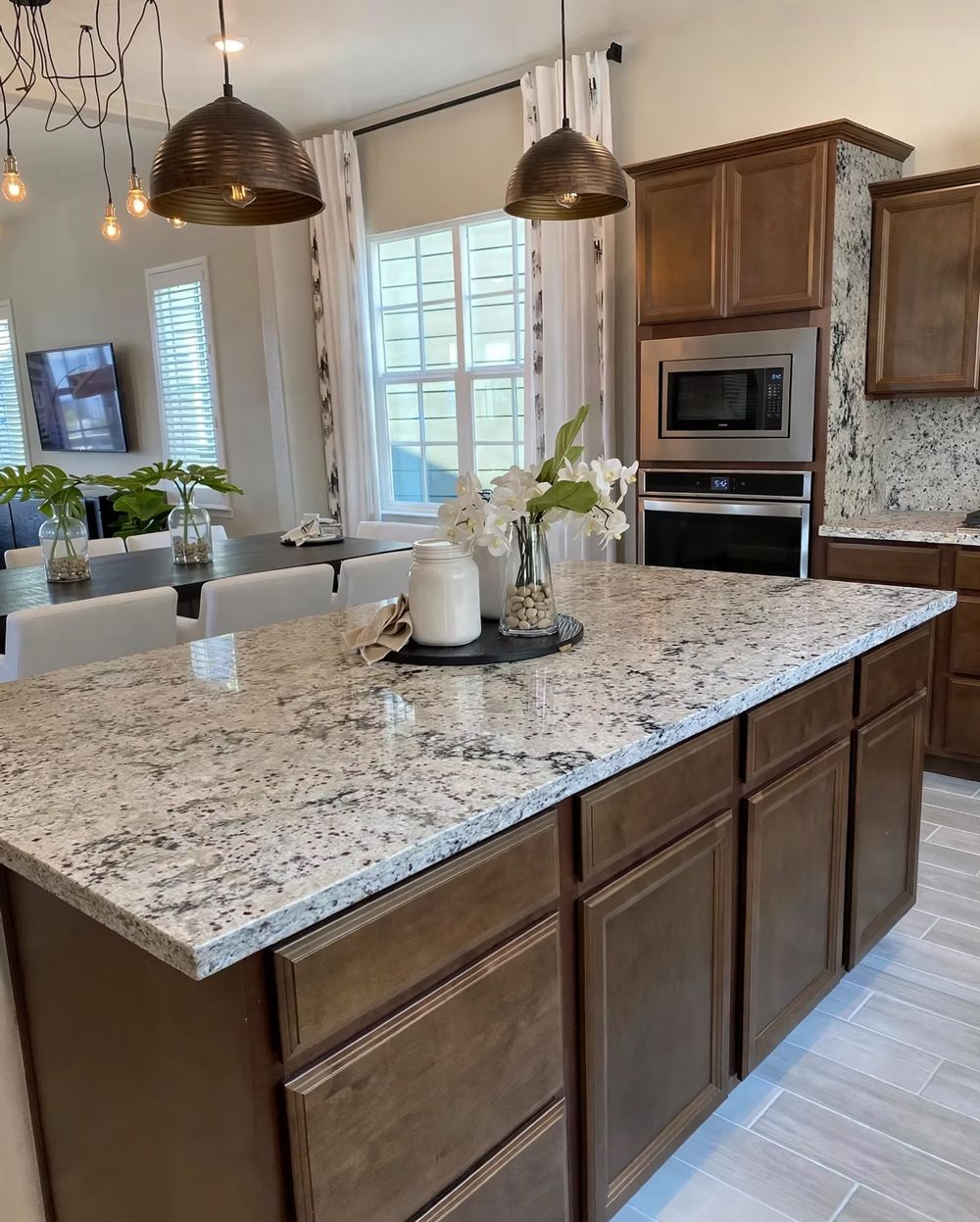 Modern kitchen with large speckled island, pendant lights, wood cabinets, and built-in oven