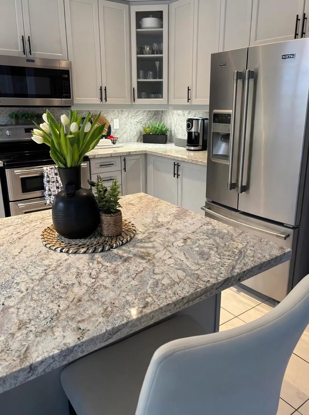 Modern kitchen with granite island, white cabinets, stainless-steel appliances, and a vase of white tulips
