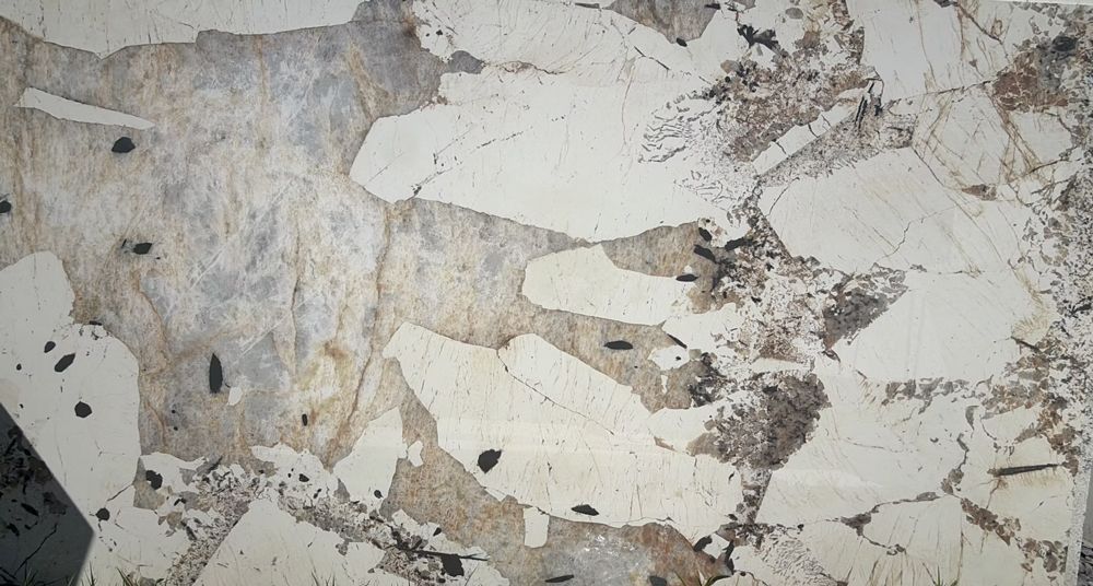 Close-up of chipped white paint peeling from a textured gray wall, revealing layered surfaces underneath.