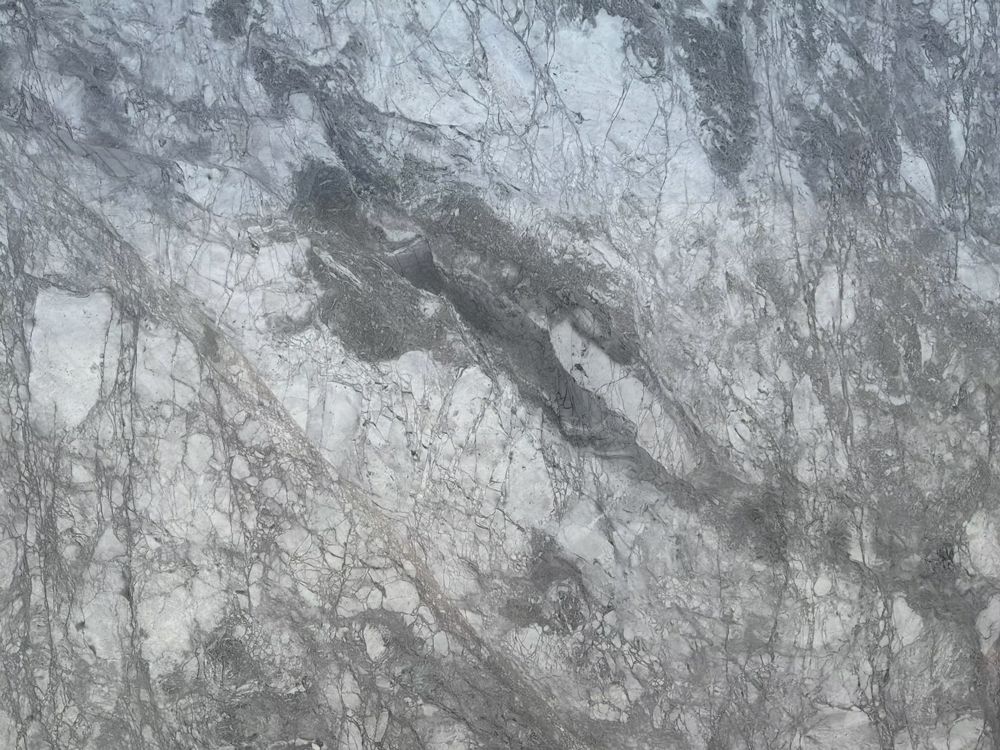 Gray and white marble-like rock surface with dark veining and textured cracks