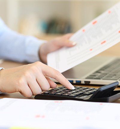 Persona que usa una calculadora mientras revisa documentos en un escritorio con una computadora portátil.