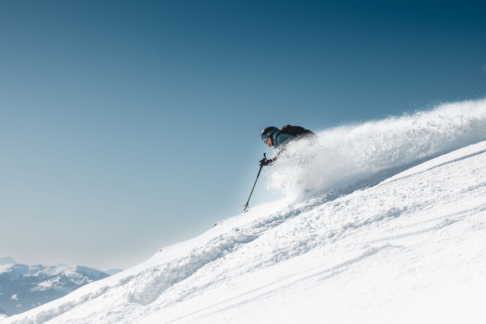 Skier carving down a snow-covered slope, creating a cloud of powder. Blue sky background.