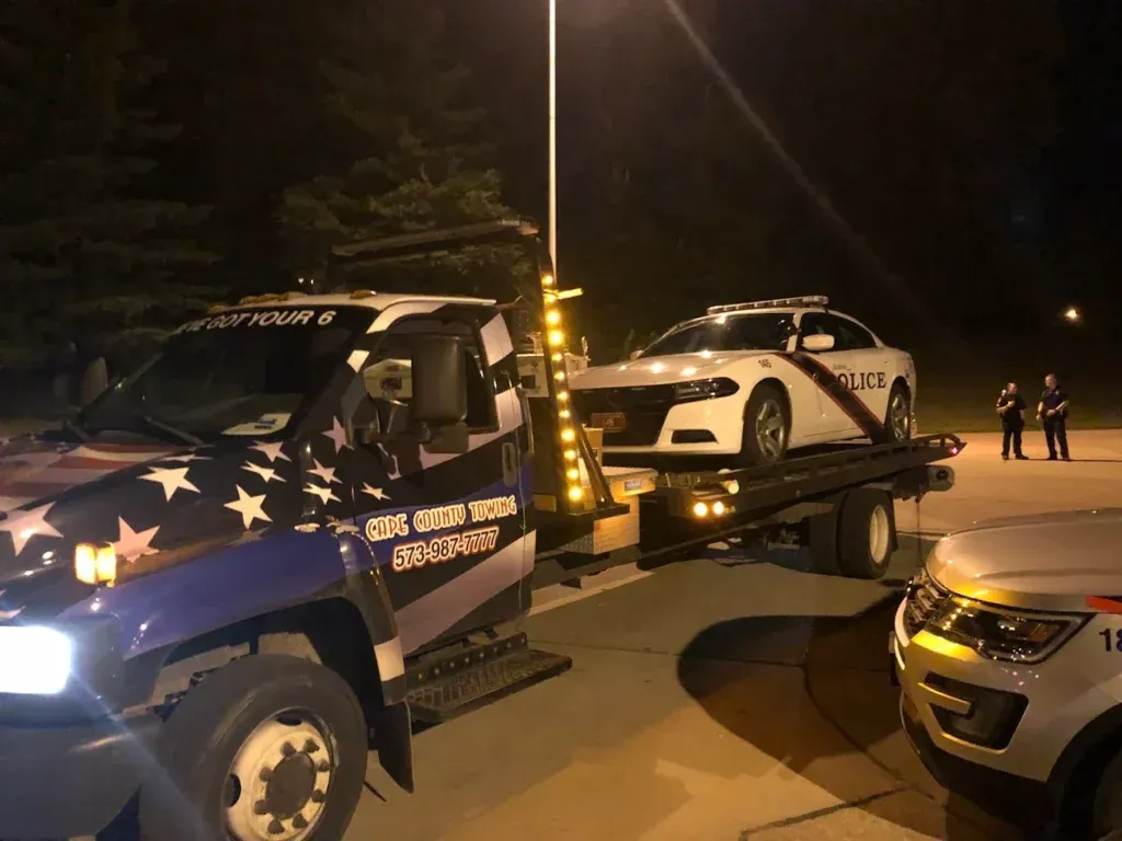 Tow truck hauling a police car at night; other police cars and officers present.