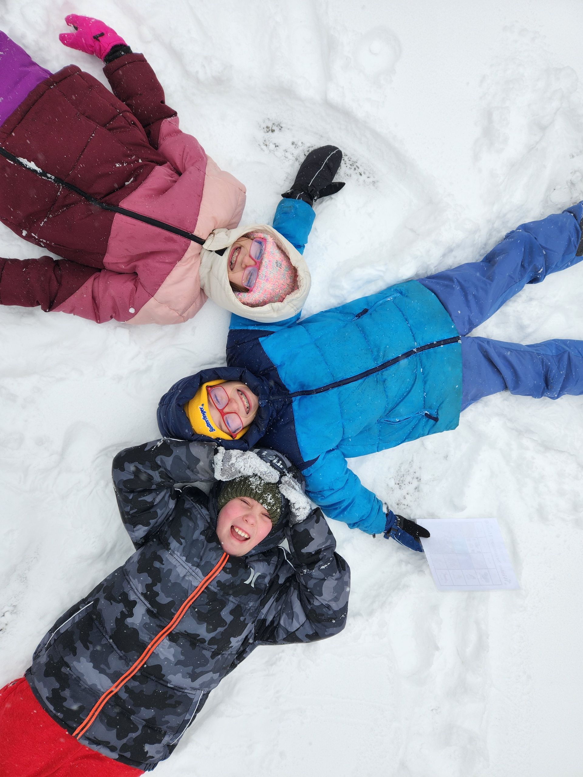 Children smiling while lying in the snow.