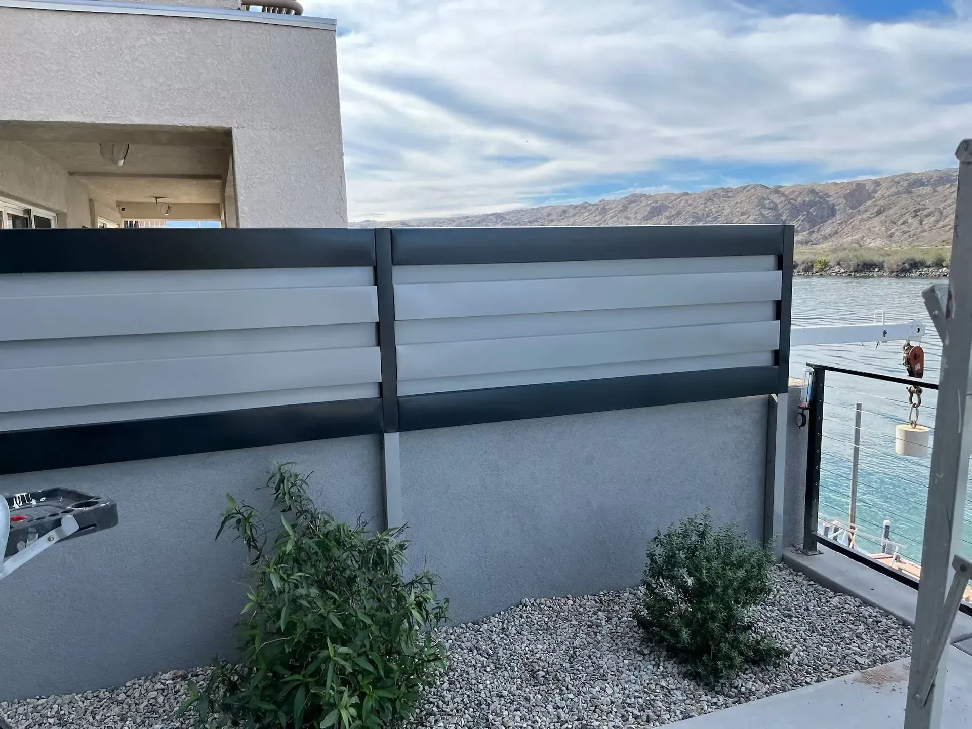 Balcony with gray privacy panels, potted plants, and a lake view beyond a rocky shoreline