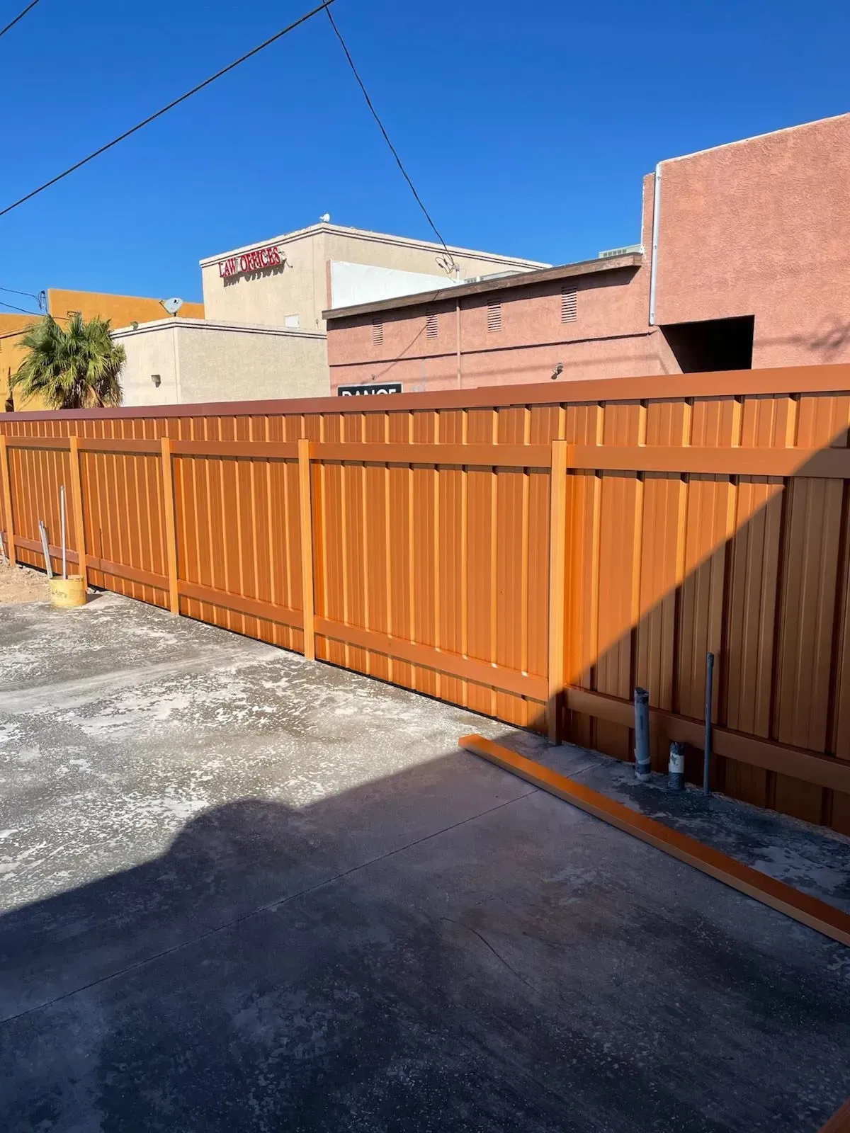 Orange fence and gate along a driveway beside tan stucco buildings under a clear blue sky