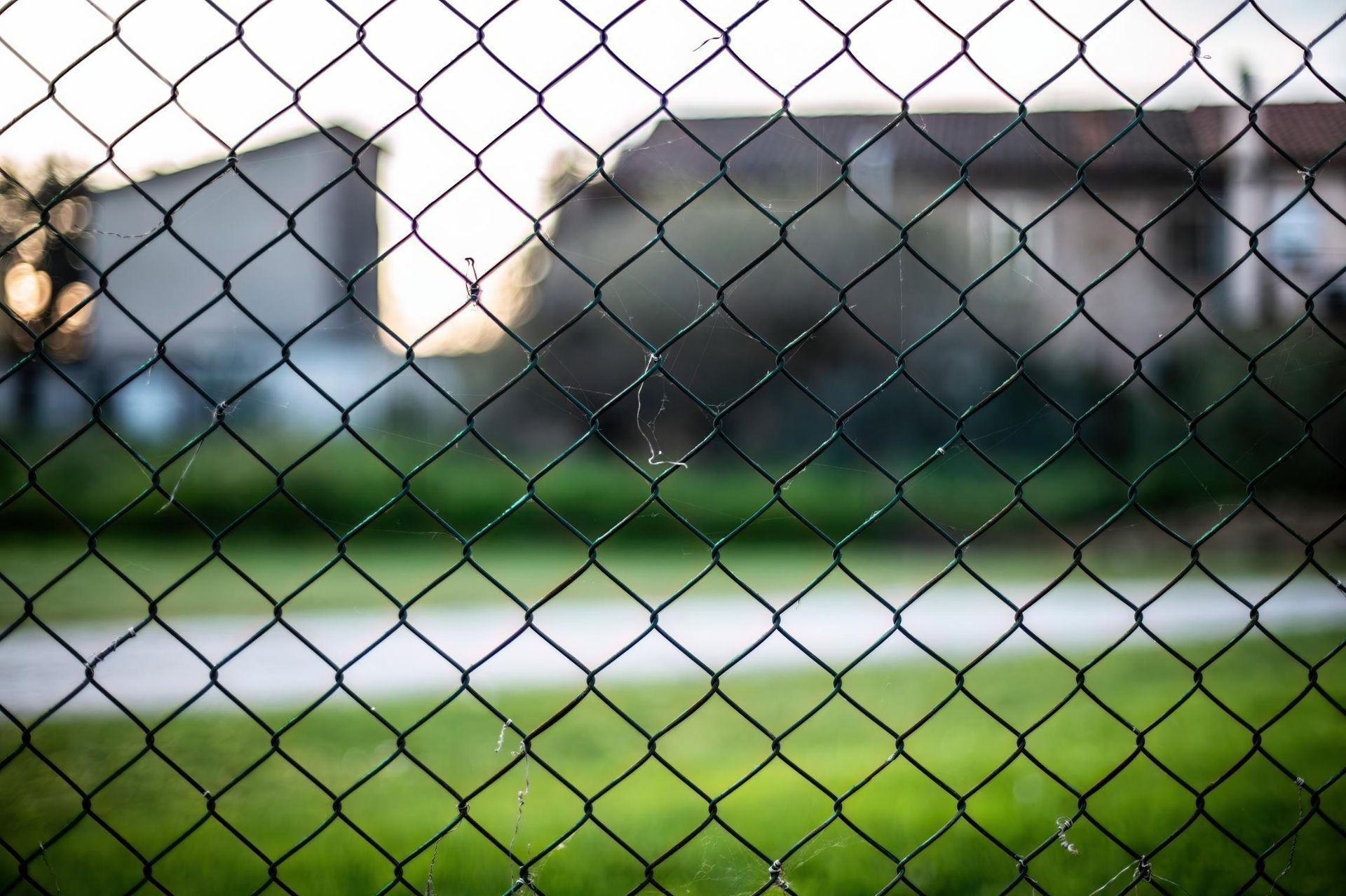 Chain-link fence overlooking a blurred suburban street and houses at dusk