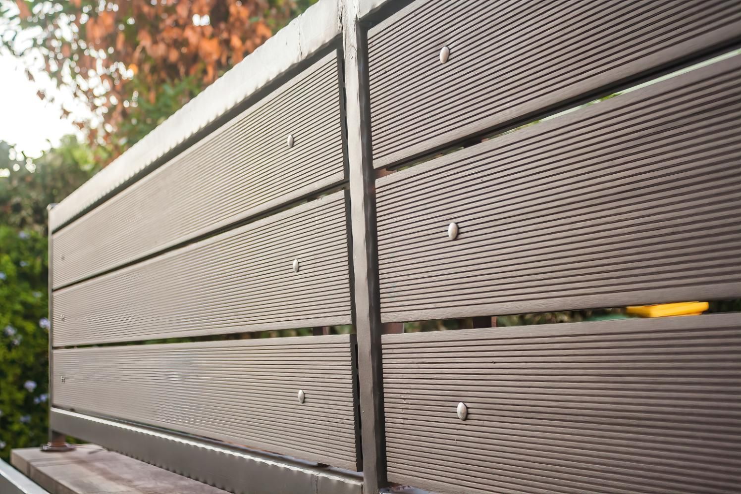 Close-up of gray metal fence panels with diagonal slats and a yellow object behind them.