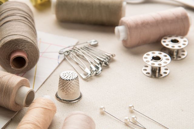 Materiale per cucire, tra cui rocchetti di filo, spilli, ditali e rocchetti, disposti sul tessuto.
