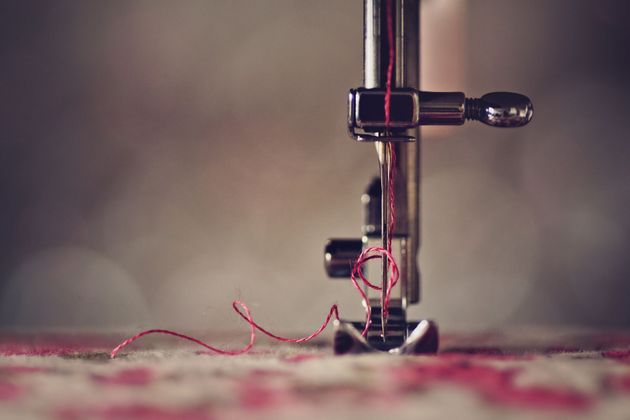 Primo piano dell'ago di una macchina da cucire con filo rosso; cucito su tessuto fantasia.