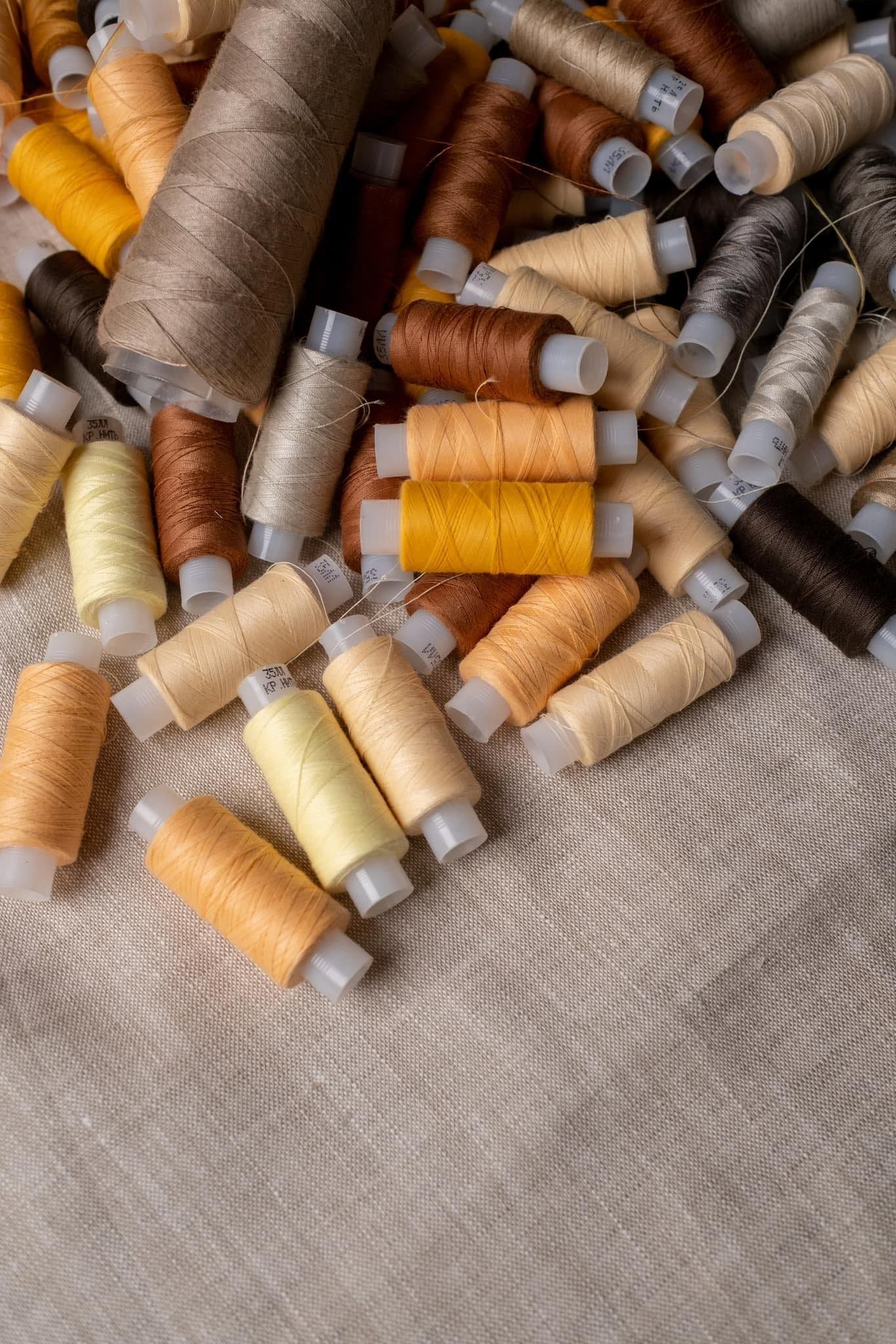 Rocchetti di filo in varie tonalità di beige e marrone su tessuto testurizzato.