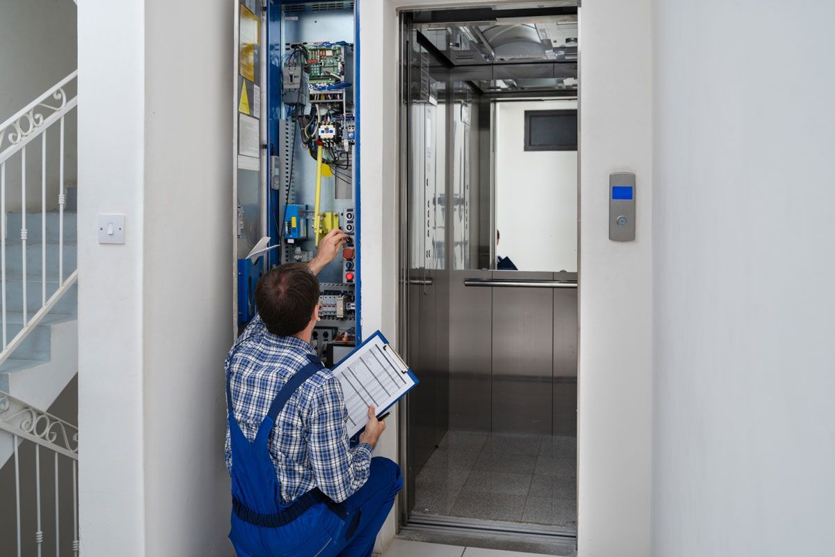 A man is working on an elevator while holding a clipboard.