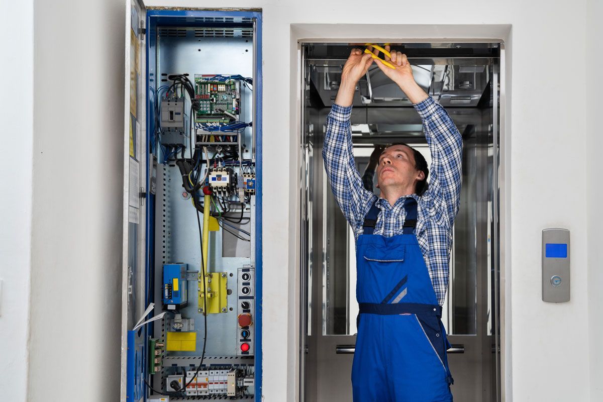 A man in blue overalls is working on an elevator