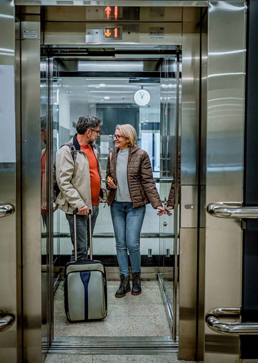 A man and a woman are standing in an elevator with their luggage.