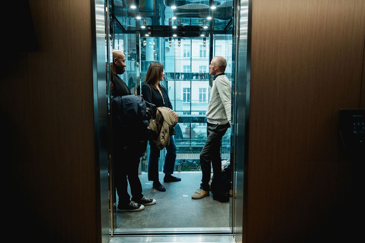 A group of people are standing in an elevator talking to each other.