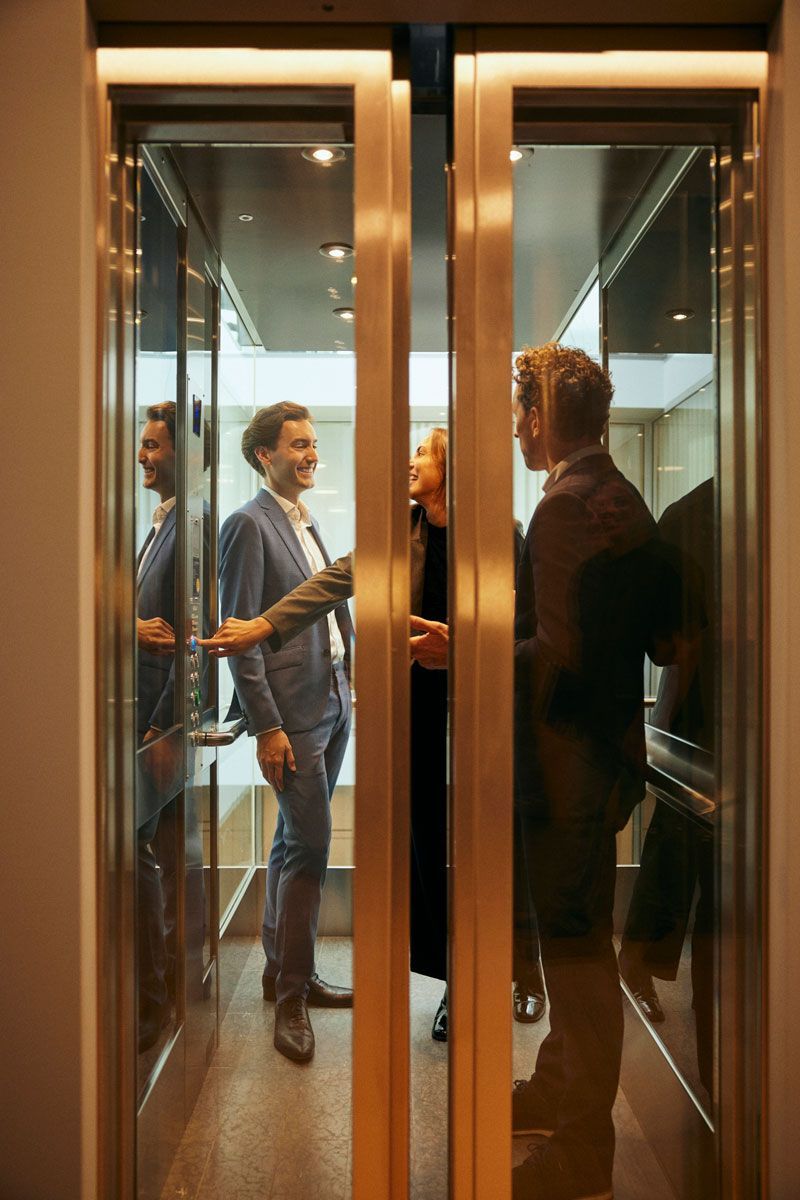 A group of people are standing in an elevator talking to each other.