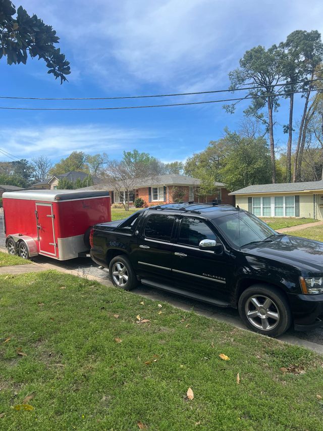 Black SUV parked beside a red enclosed trailer in a suburban driveway on a sunny day