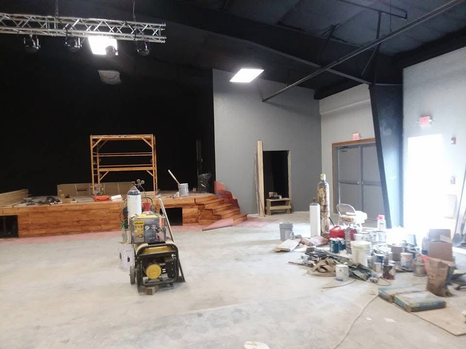 Empty indoor construction site with concrete floor, scaffolding, tools, and building materials under bright lights