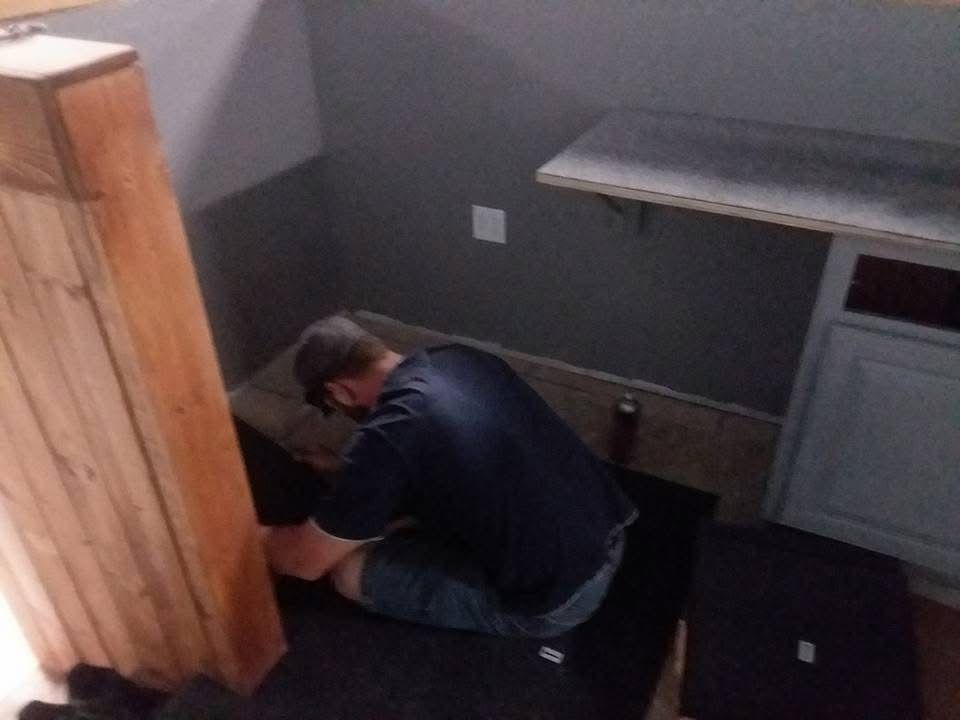 Person crouching on a kitchen floor beside cabinets and a countertop, working near the wall.