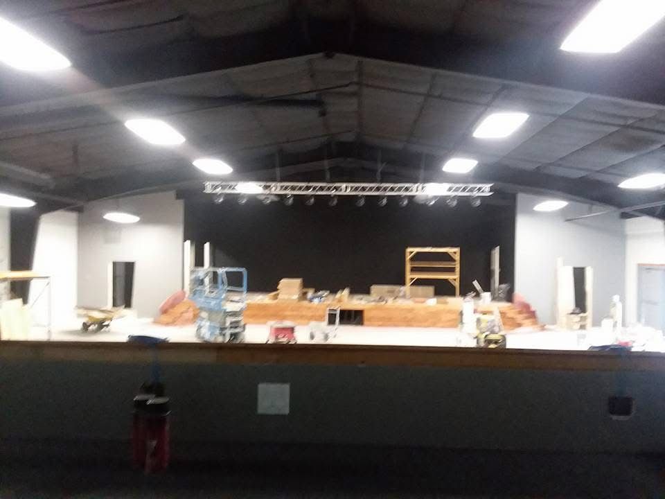 Empty indoor stage with equipment, lights, and construction materials under a high ceiling