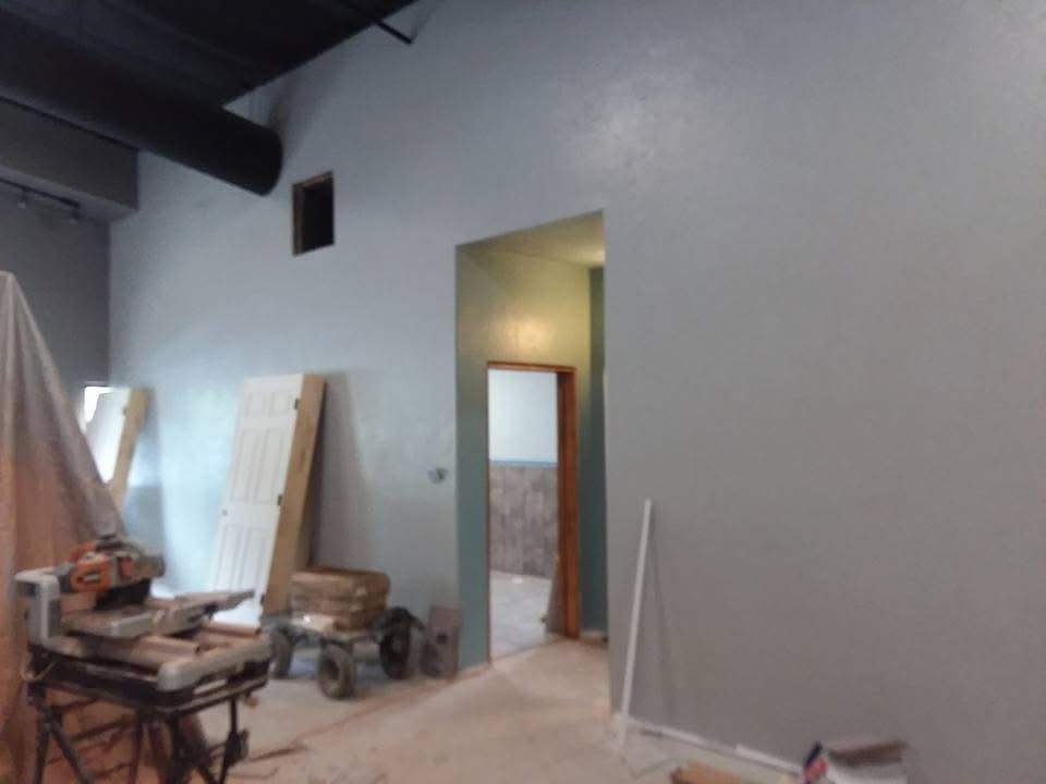 Empty room under renovation with drywall, tools, and stacked boards near an open doorway