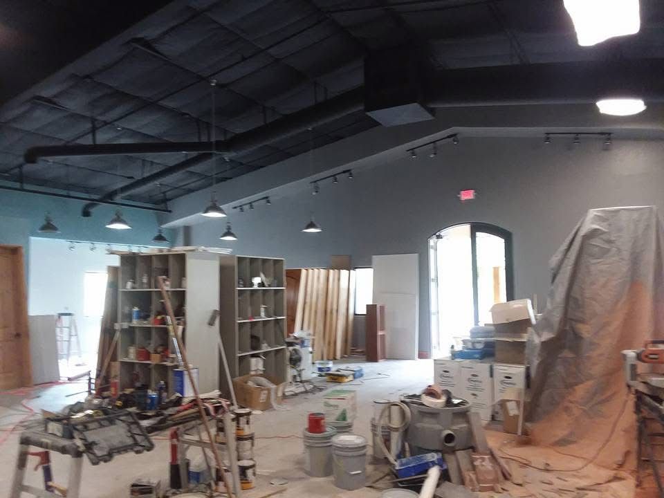 Renovation site with ladders, tools, paint buckets, and covered equipment inside a partially finished room