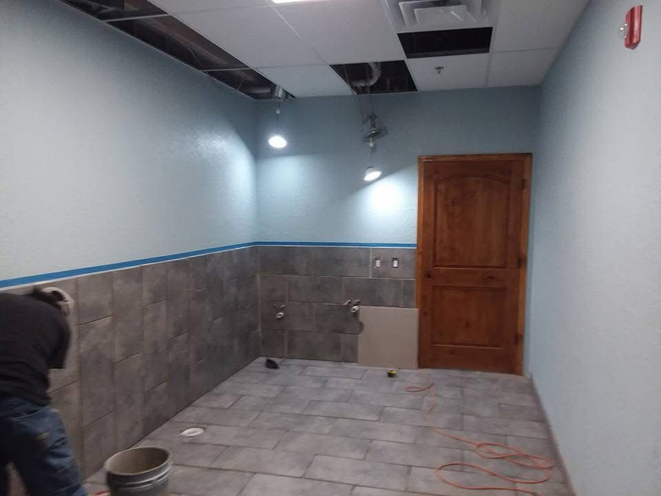 Partially tiled room with blue walls, wooden door, and a person working near a bucket on the left